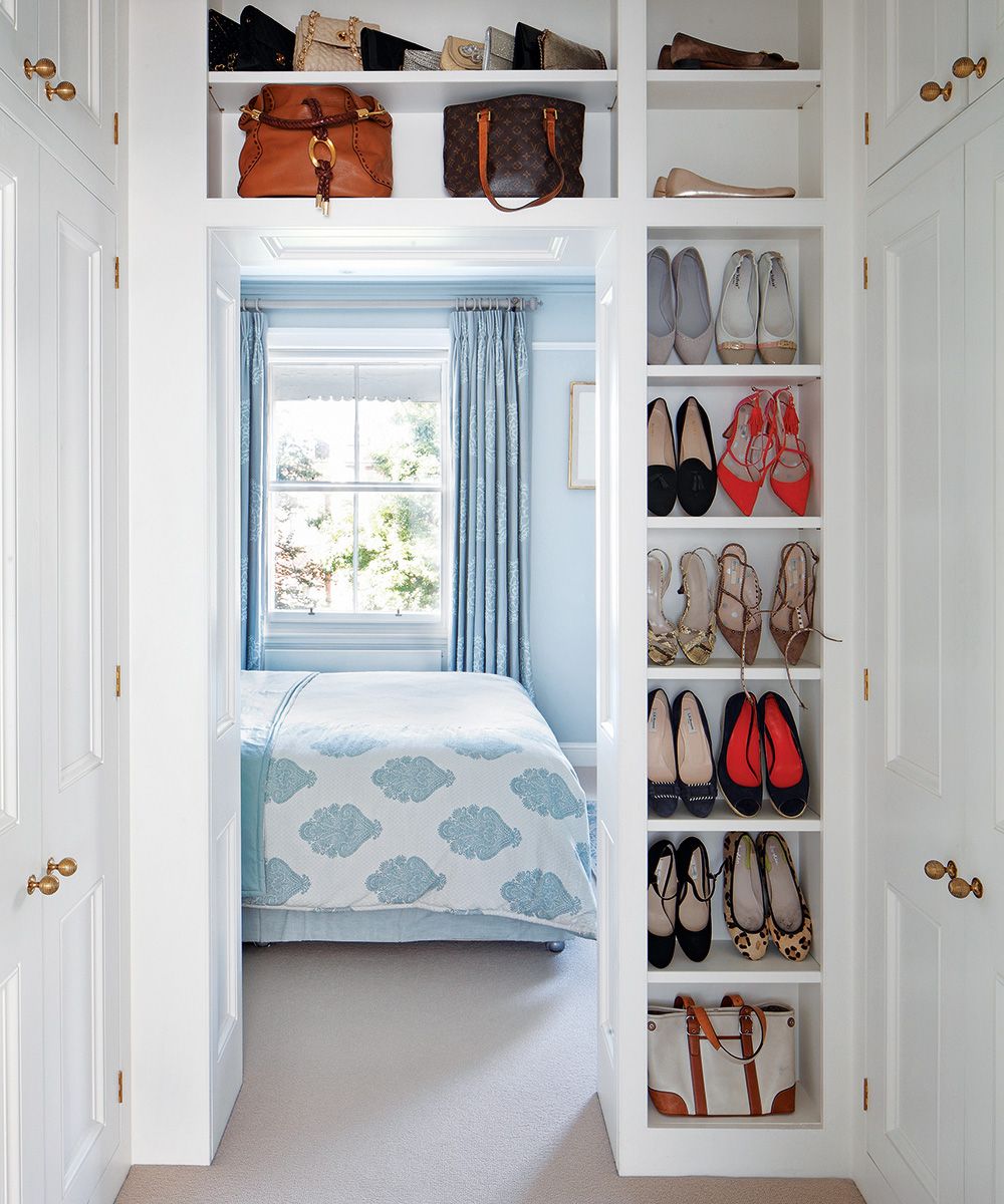 White shoe storage surrounding the doorway to a small pale blue bedroom.