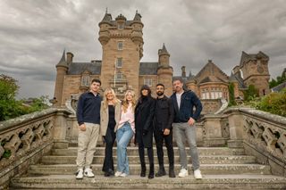 The Traitors Series 2 finalists standing on the steps outside the castle with Claudia Winkleman in their everyday clothes. From left to right: Harry Clark, Evie Morrison, Mollie Pearce, Claudia Winkleman, Jaz Singh, Andrew Jenkins.