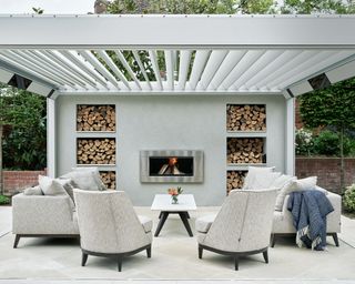 Built-in outdoor fireplace ideas with pale gray outdoor seating below a white pergola.