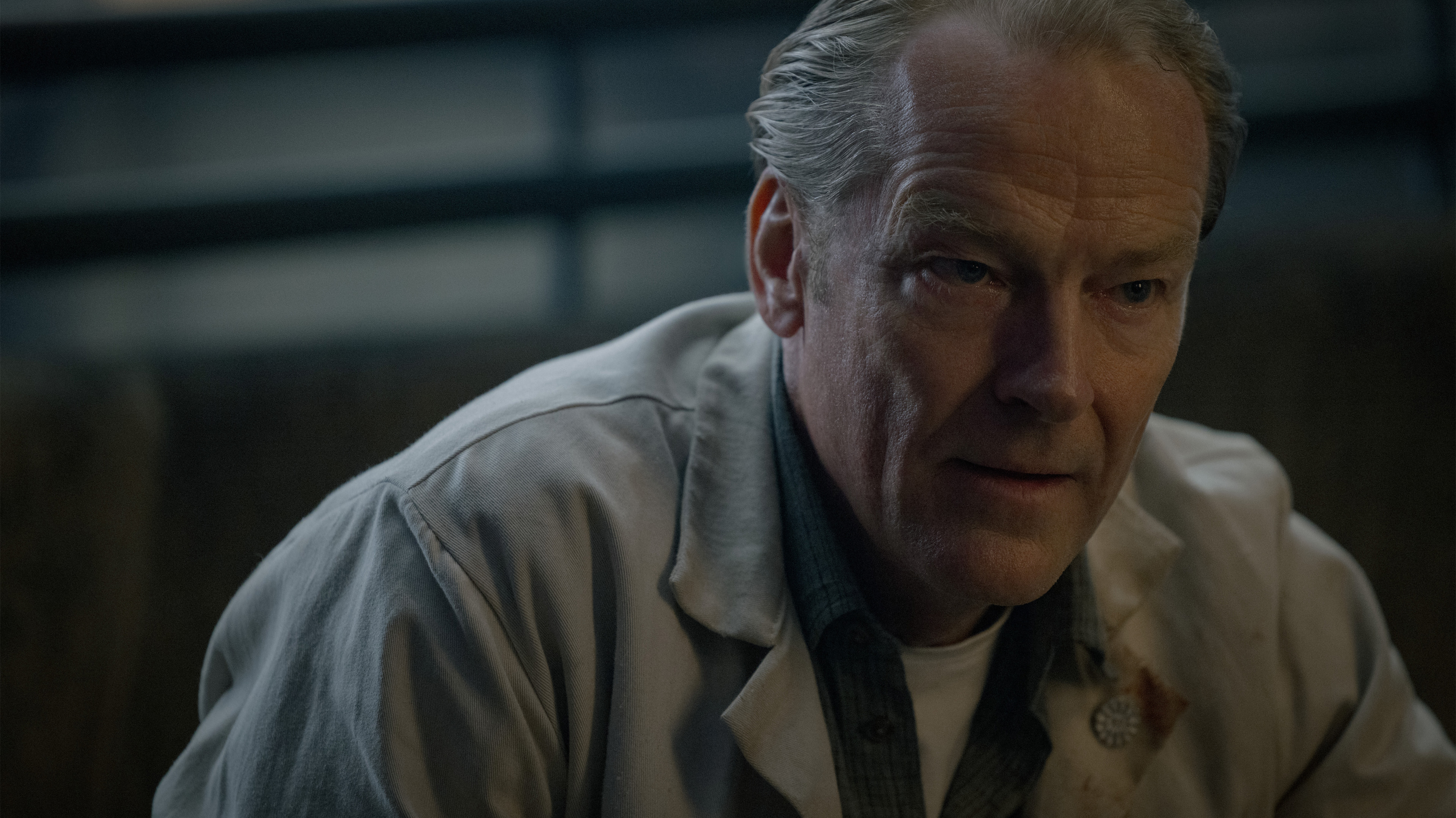 An older man in a jacket crouches in a stairwell