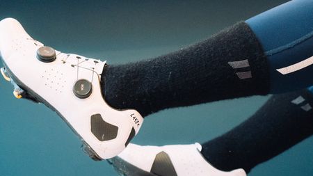 A man wears a set of white cycling shoes, black fluffy socks, and blue tights against a blue background