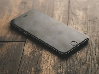 A Jet Black iPhone 7 rests on a wooden table or floor.