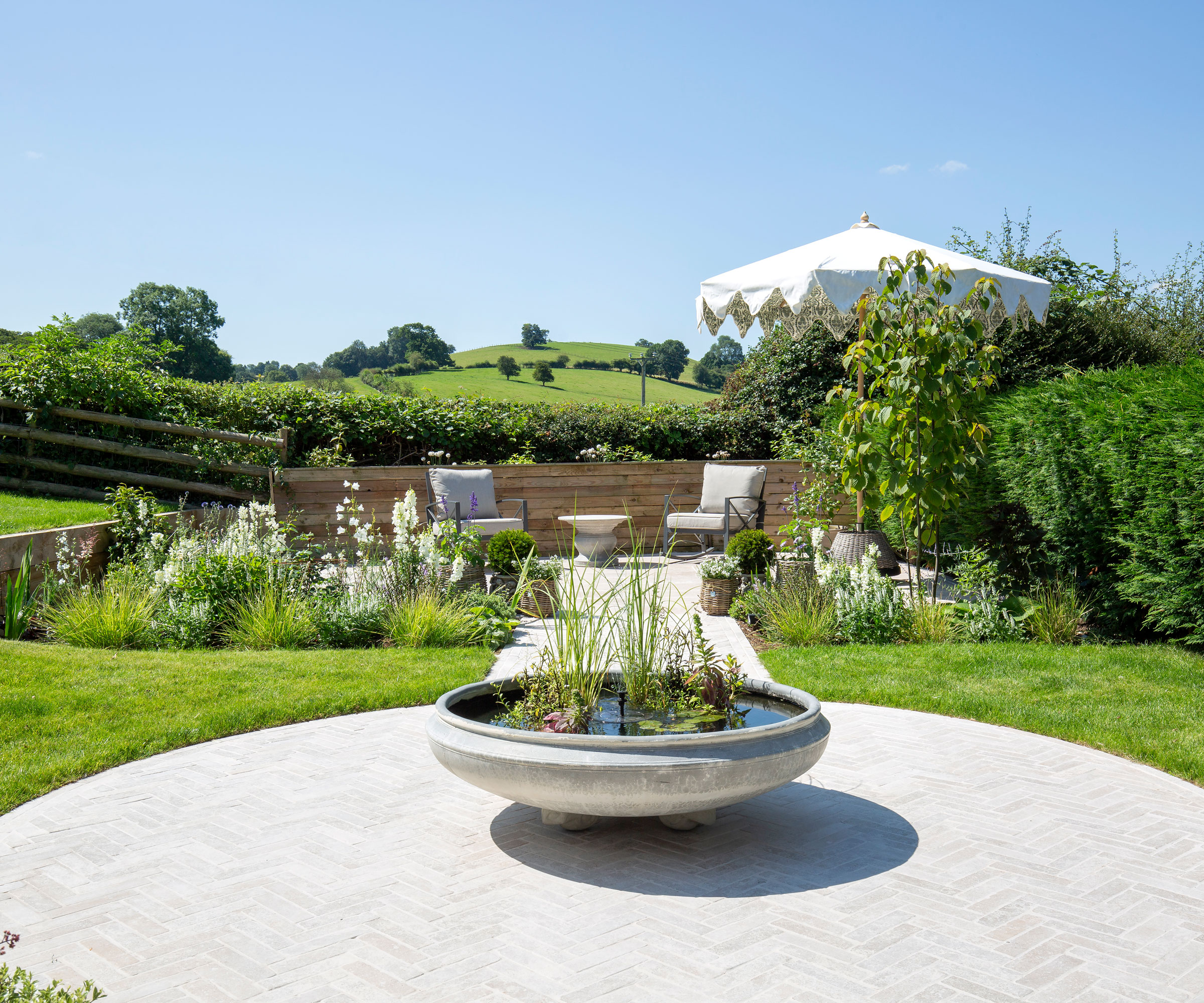 circular patio with water feature and path leading to second patio with garden furniture and umbrella