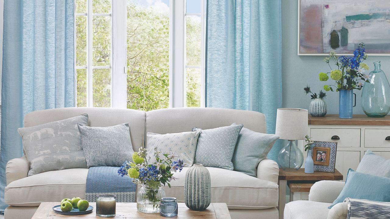 A living room with light blue curtains and matching throw cushions on a light grey sofa