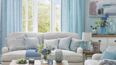 A living room with light blue curtains and matching throw cushions on a light grey sofa