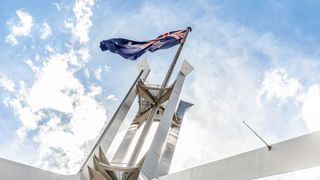A shot of the Australian flag flying above a building with a blue sky in the background