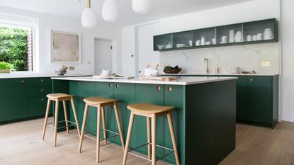 green and white kitchen with green island, white worktop, narrow glass fronted wall units, oak wood bar stools