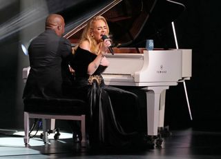 Adele on stage sitting on a piano stool