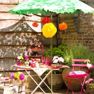 small garden with circular table pink metal chair green parasol and pink tableware