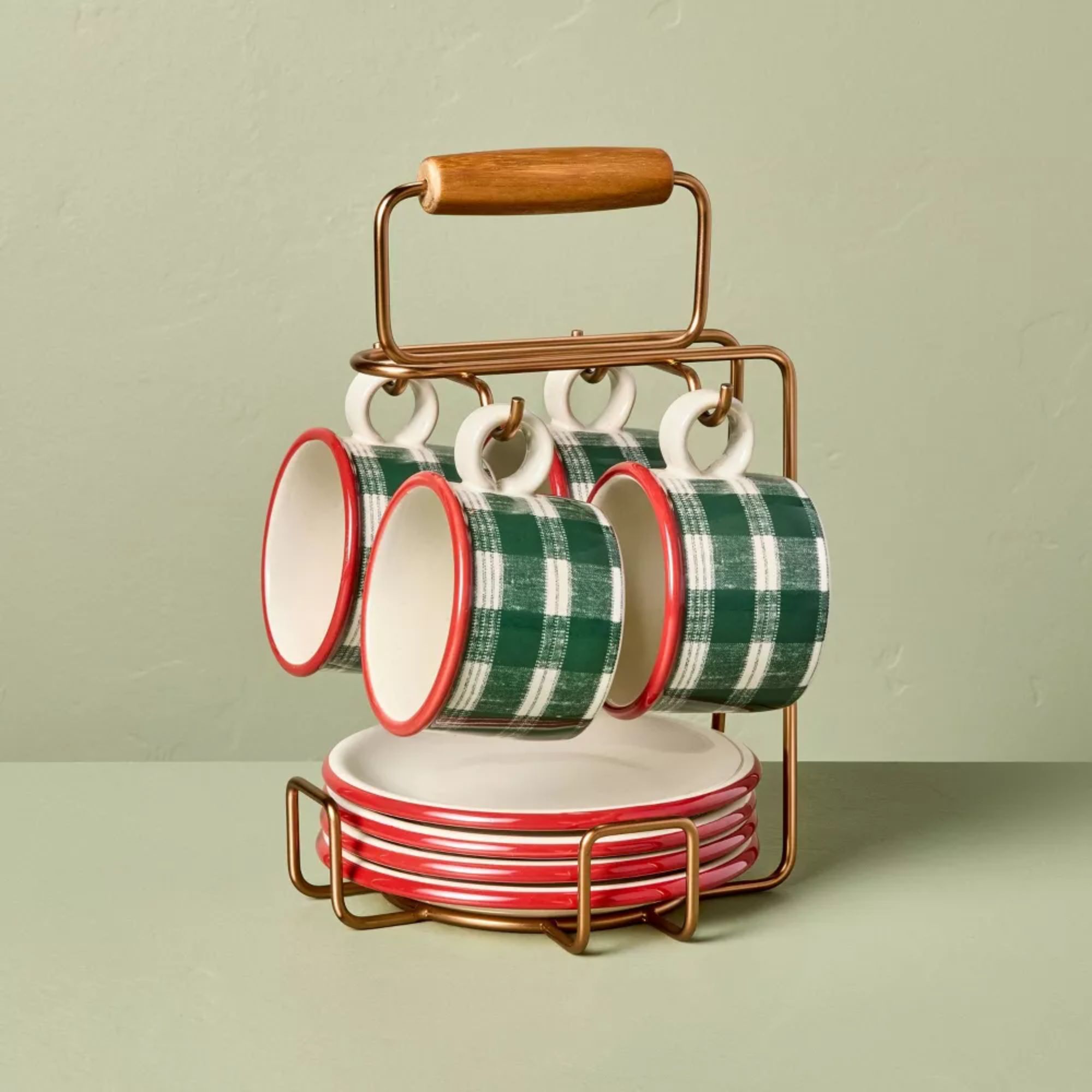 Brass caddy holding red and white plates and green and white plaid-style mugs
