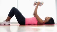 Woman doing the chest fly exercise on the floor with a pair of dumbbells