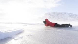Hiker photographing the arctic sunrise lying down on frozen lake