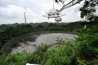 The Arecibo Observatory sustained serious damage during Hurricane Maria. The pointy object protruding downward from the suspended platform is a 96-foot (29-meter) antenna that broke off during the hurricane, puncturing the telescope dish below.