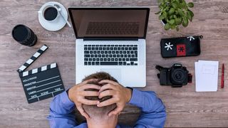 Frustrated person with hands on head, hunched over laptop