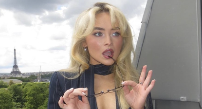 Sabrina Carpenter poses with glasses in front of the Eiffel tower wearing a pinstriped set