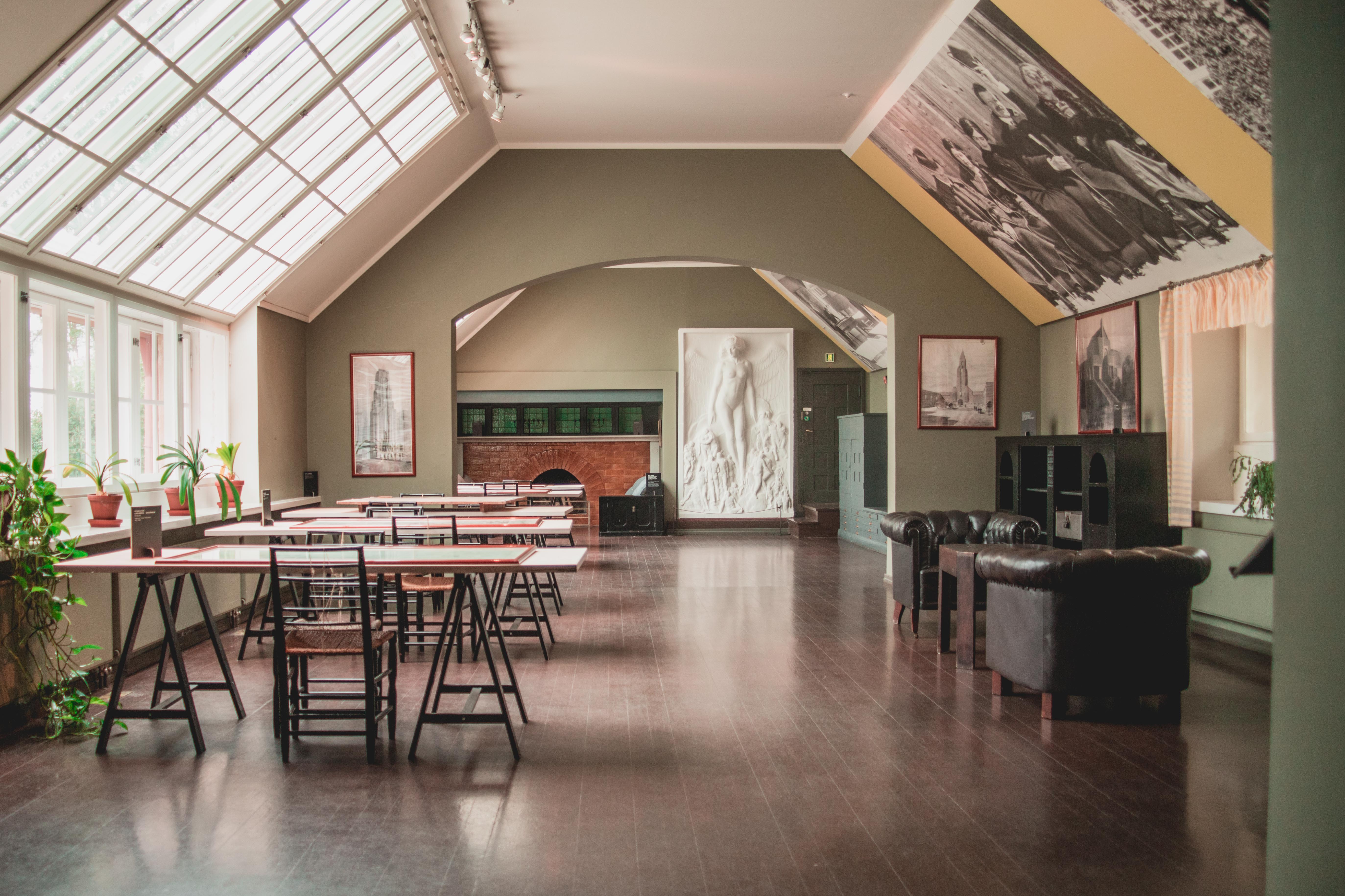 A naturally lit design studio with wooden floors, thriving plants, a chalk relief depicting a human silhouette, and other framed artworks, brought to life by the light filtering through its glass windows.