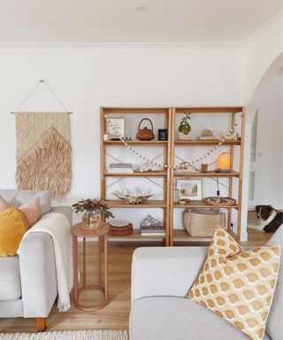 A small living room with two couches and two wooden bookshelves with decor