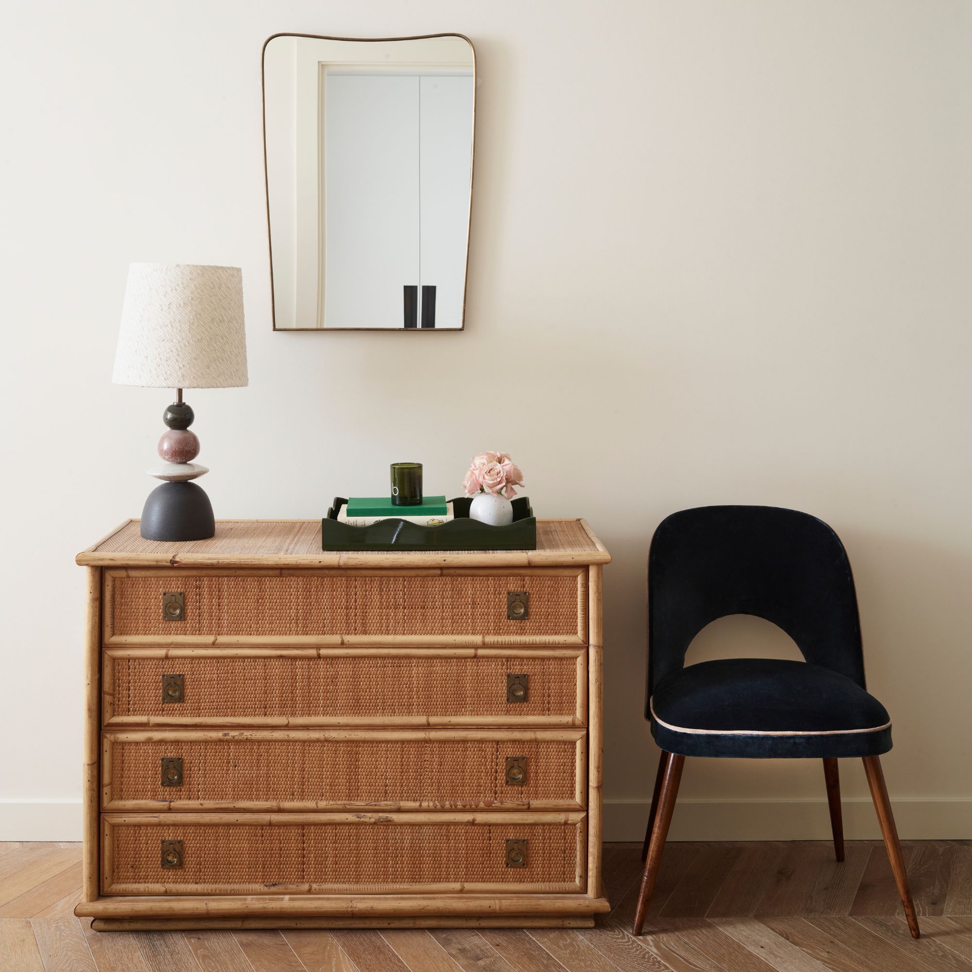 Bedroom with neutral colour walls, reeded chest of drawers, black velvet chair and a mirror and lamp