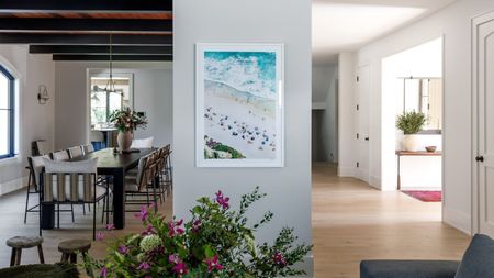 Open plan living space showing dining room on left, entryway on right with florals and artwork