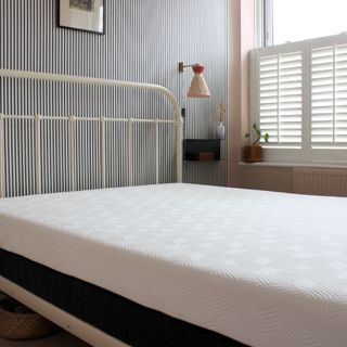 A mattress on a bed with a white bed frame in a room with pink walls and black and white striped feature wall