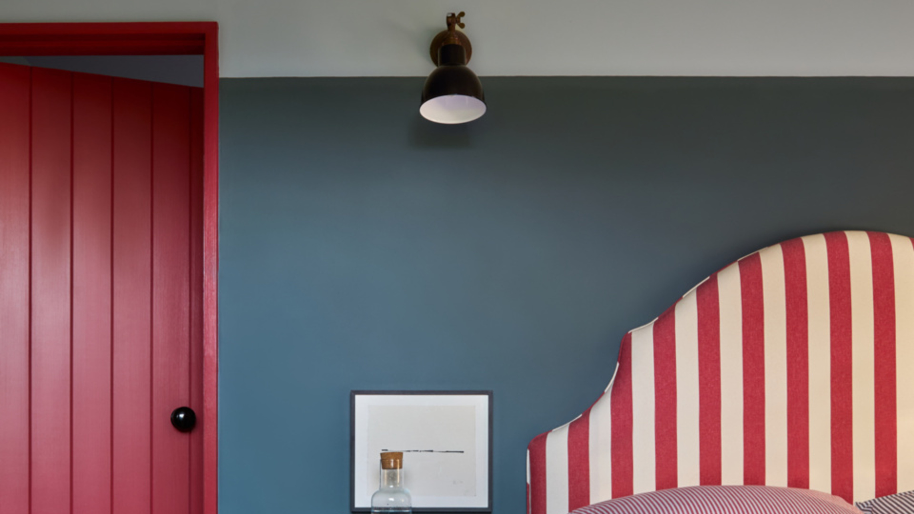 A bedroom with blue walls, and red and white striped headboard, and red door trim 