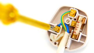 Yellow screwdriver wiring a white 3-pin plug