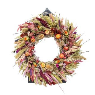 A fall wreath with purple, pink, green, and orange dried grass and flowers on it