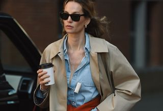 Woman wearing a tan trench coat over a light-wash denim button down.