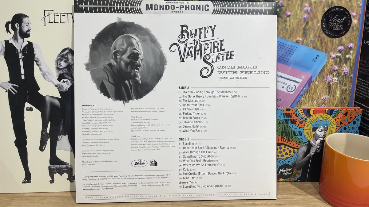 The back cover of Once More With Feeling on vinyl. It's white with black text. There are more records in the background and an orange mug to the right.