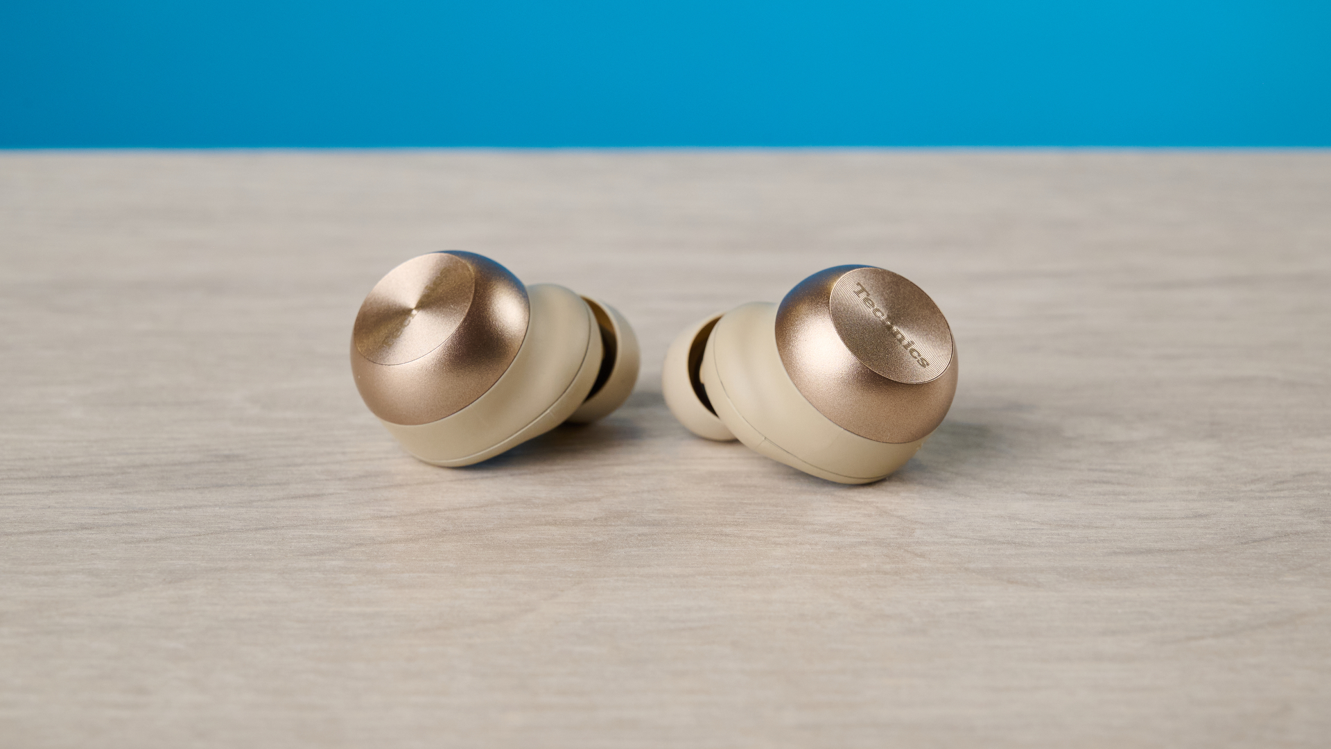 the technics az100 earbuds in champagne photographed against a blue tom's guide background