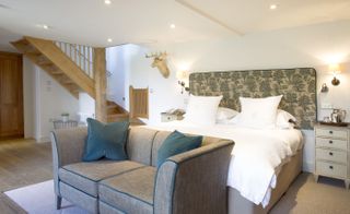 Bedroom in Calcot Manor, Gloucestershire, UK with fabric headboard, white bedding, sofa and wooden staircase