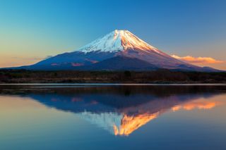 Mount Fuji is reflected in the water at sunset