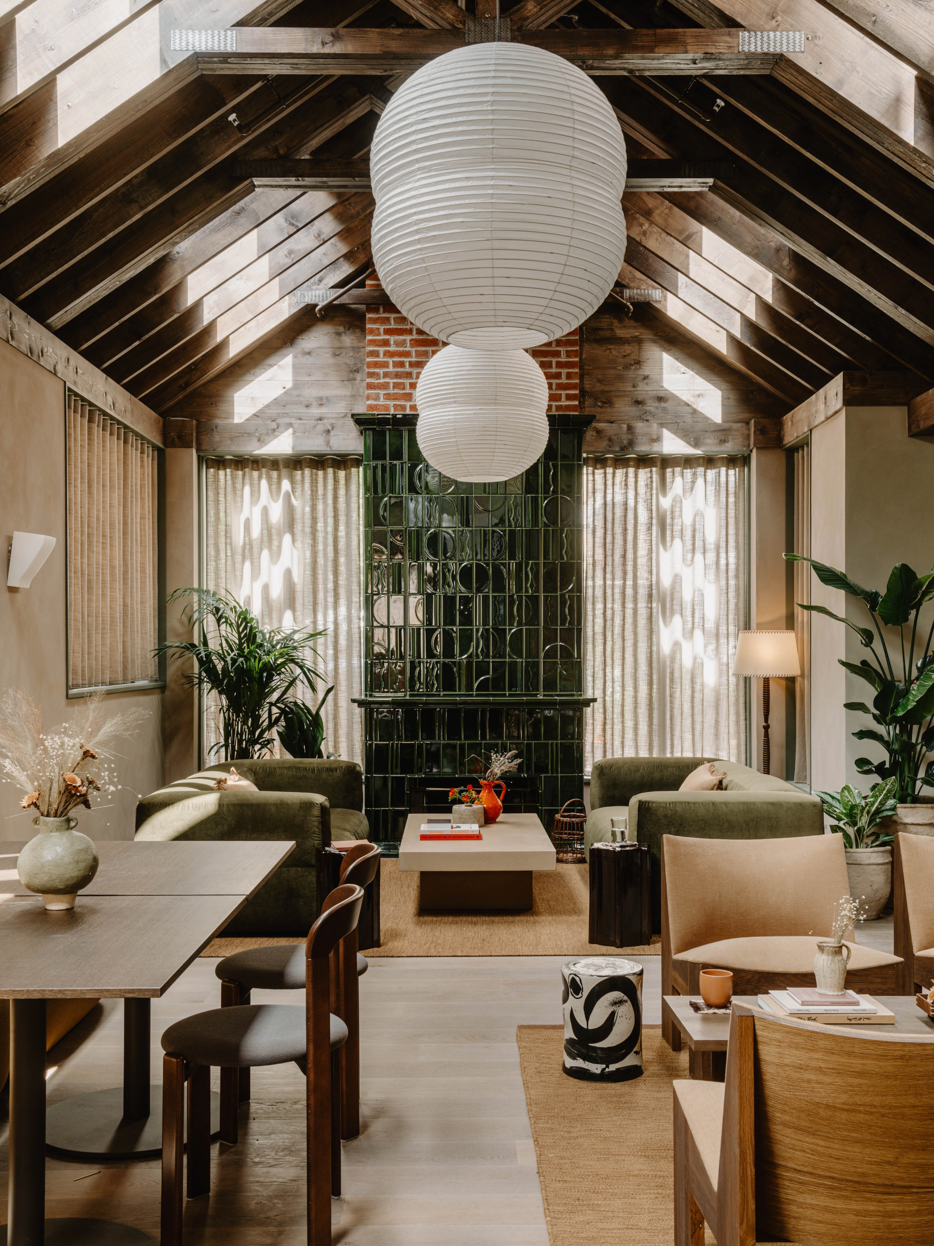 Living area of Mason &amp;amp; Fifth Belsize Park with green tiled fireplace, red and pink geometric art, two striped armchairs, brown sofa with dining table and chairs, white coffee table and wooden unit