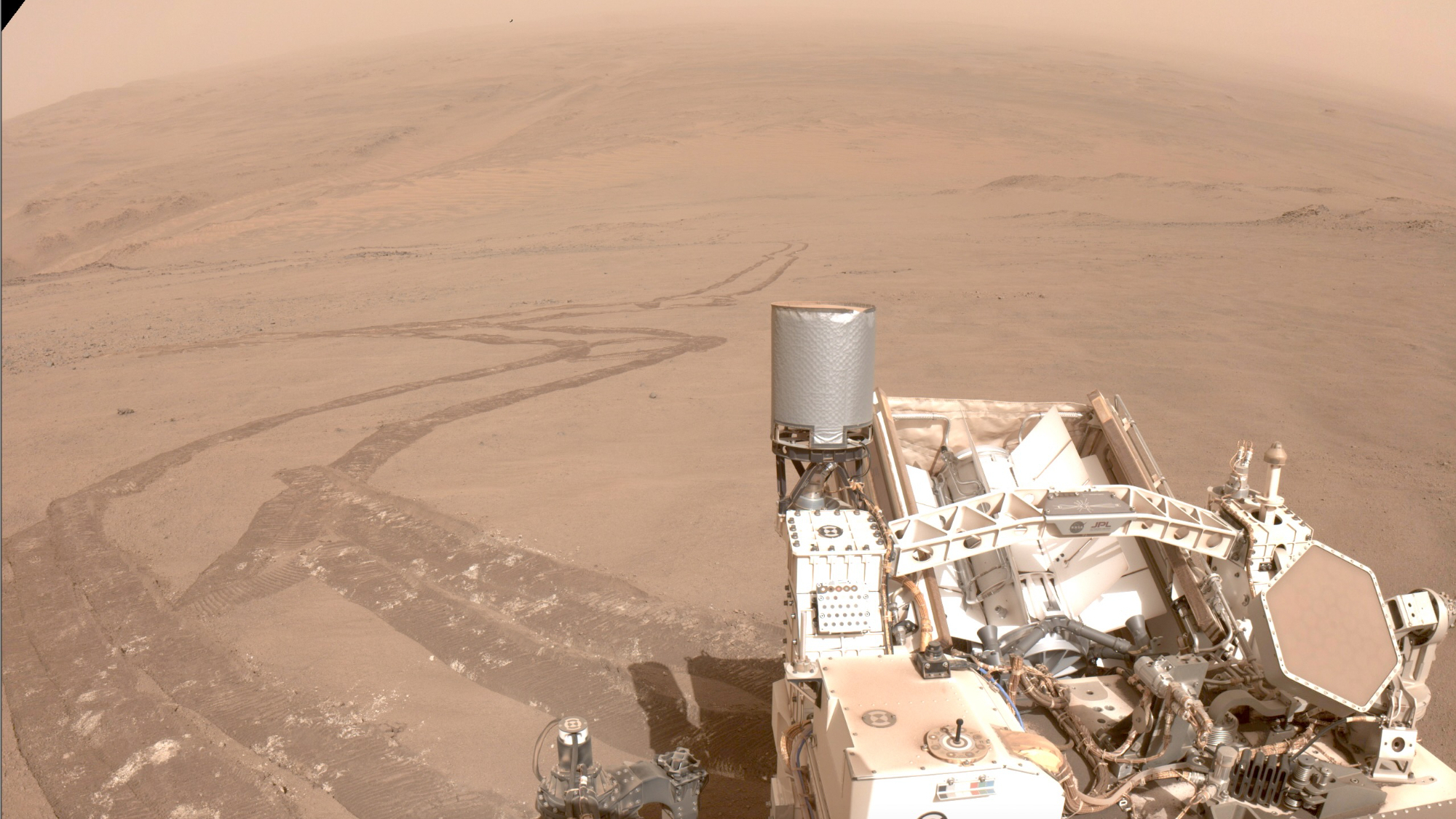 A photo of the Mars Rover in the foreground, its orbit extending far into the red dirt.