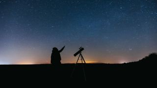 A person with a telescope in silhouette against the night sky