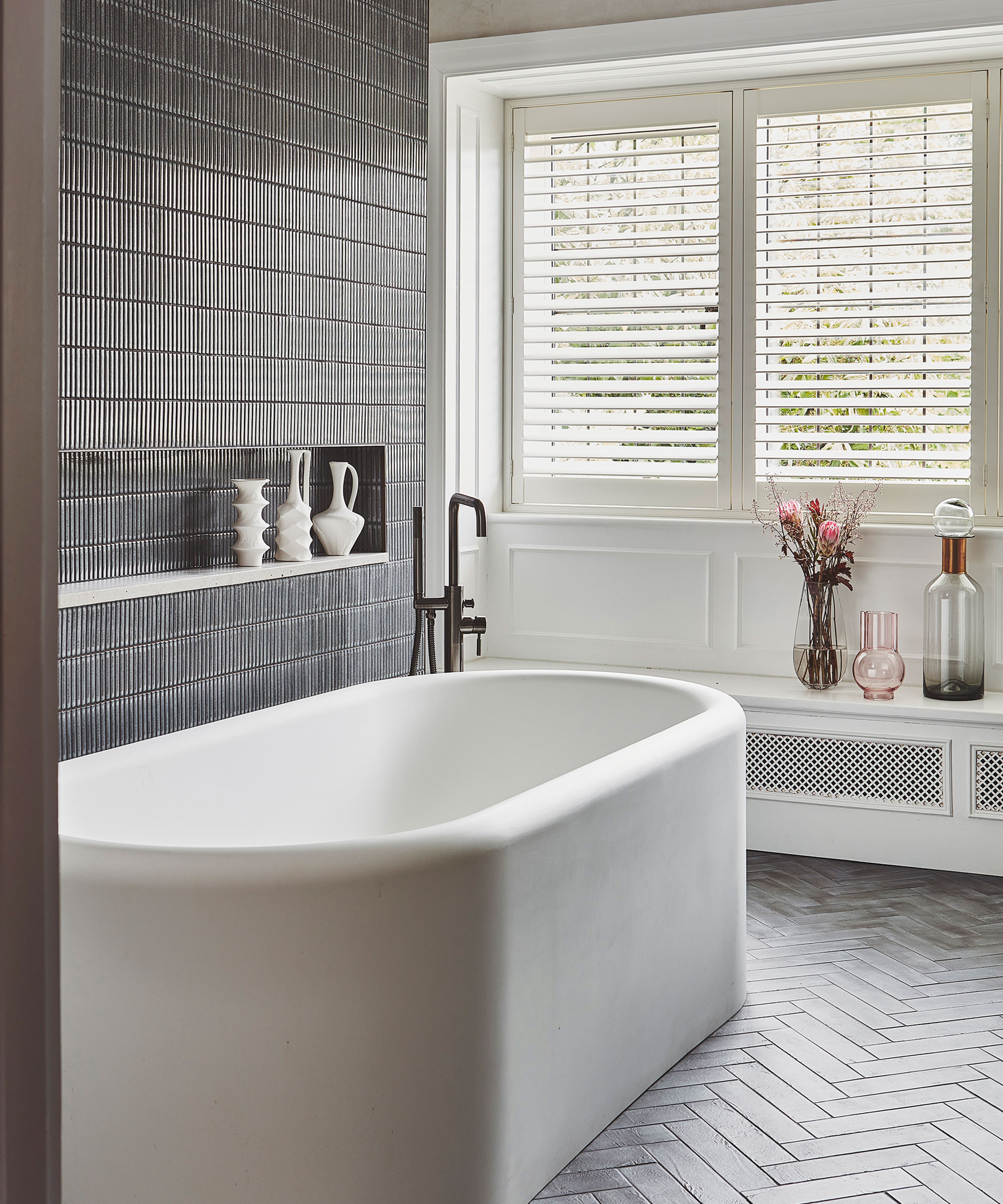timeless bathroom with modern freestanding bath and herringbone flooring with white window shutters