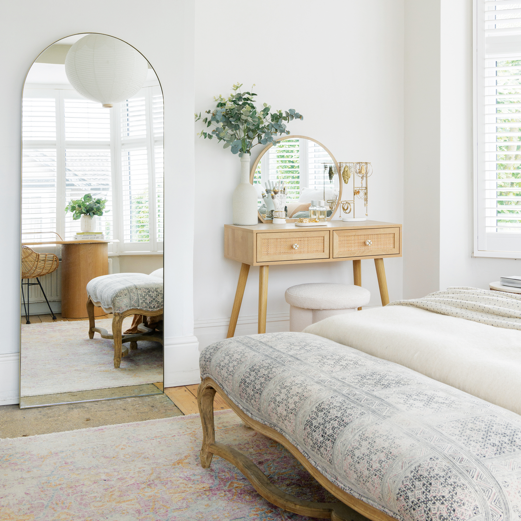 a neutral coloured bedroom with a wooden bed frame, wooden dressing table and curved top floor length mirror