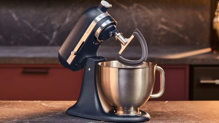 A dark blue 'wild blueberry' stand mixer with a stainless steel bowl on a dark stone worktop. 
