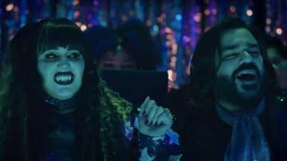 Natasia Demetriou and Matt Berry sitting in a neon lit club in What We Do In The Shadows.