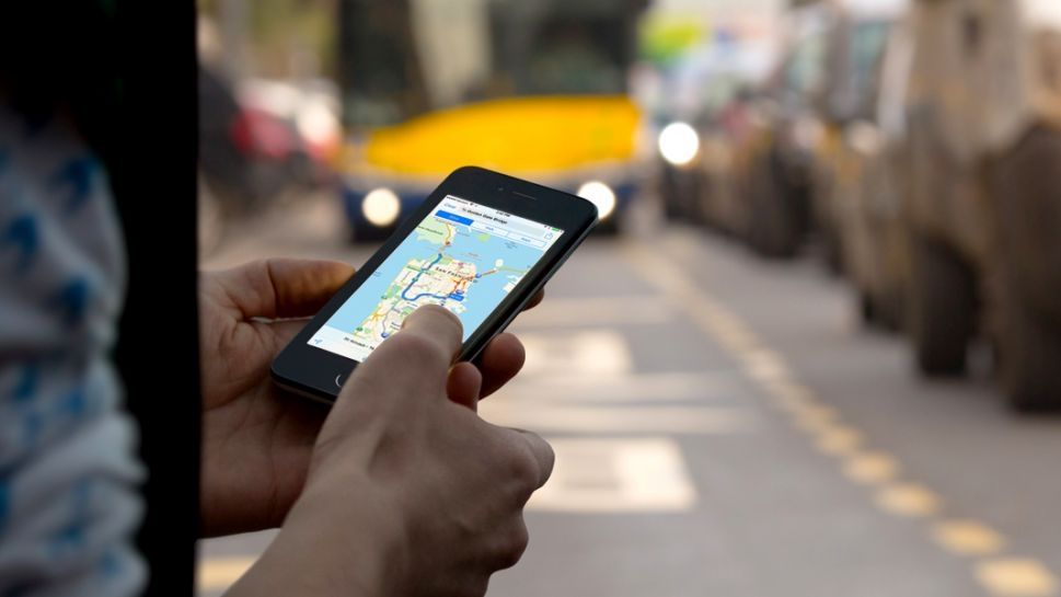 Person standing in the street, holding an iPhone with Apple Maps on the screen