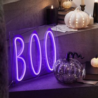 Bright purple neon boo sign switched on with glass pumpkin beside 