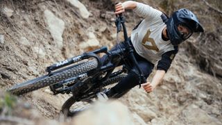 A female asian mountain biker rides a berm and leans almost horizontally. She's wearing the new Asym jersey from YT.
