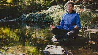 Man meditating outside near a lake