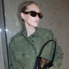 Model Elsa Hosk wears blue straight-leg jeans with a suede khaki funnel neck jacket and purple pointed-toe heels.