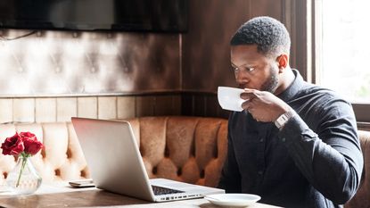 Man drinking a cup of coffee whilst working on a laptop