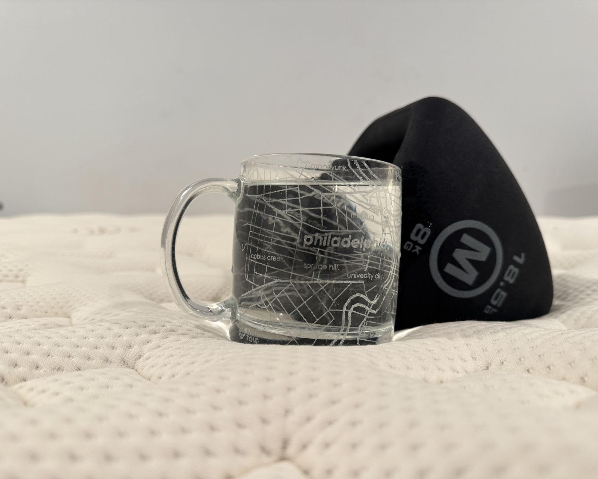 A glass with a large handle and a black weight pictured on top of the Saatva RX mattress surface.