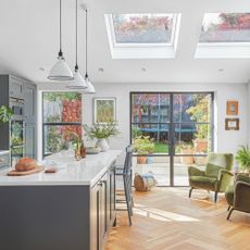 Open plan kitchen and living space with dark grey cabinets and a kitchen island, with accent chairs in the space beside it