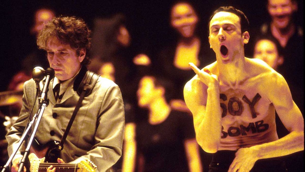 Bob Dylan onstage next to a shirtless stage invader with &#039;Soy Bomb&#039; daubed on his chest