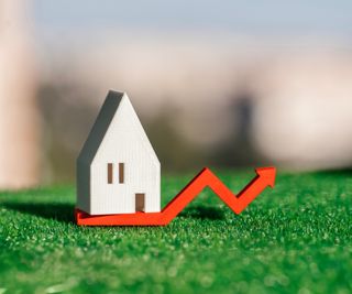 grass with wooden house model on top of red arrow rising upwards