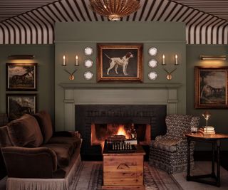 muted pale green painted hotel lounge area with a burgundy striped wallpapered ceiling and a working fireplace surrounded by comfy chairs and vintage decor